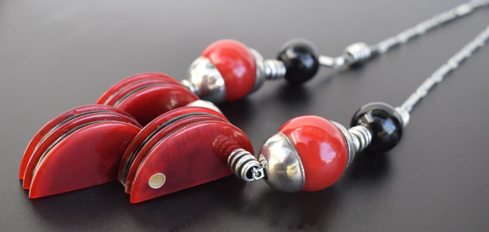 An Art Deco modernist necklace featuring red and black spherical beads, coiled silver-toned metal spacers, and a geometric central pendant composed of stacked red and black discs on a metal link chain. View VII
