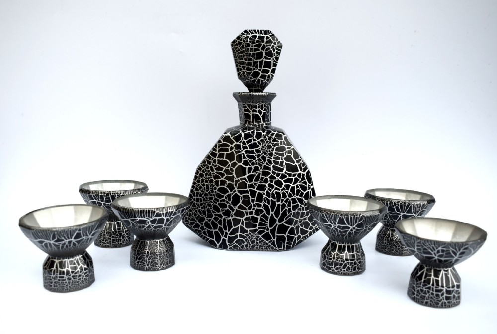 An Art Deco black and silver crackle-patterned glass decanter with six matching small cups arranged on a circular mirrored tray with wood handles. View II