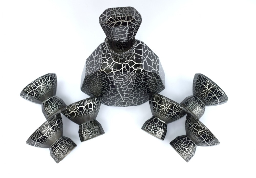 An Art Deco black and silver crackle-patterned glass decanter with six matching small cups arranged on a circular mirrored tray with wood handles. View IX
