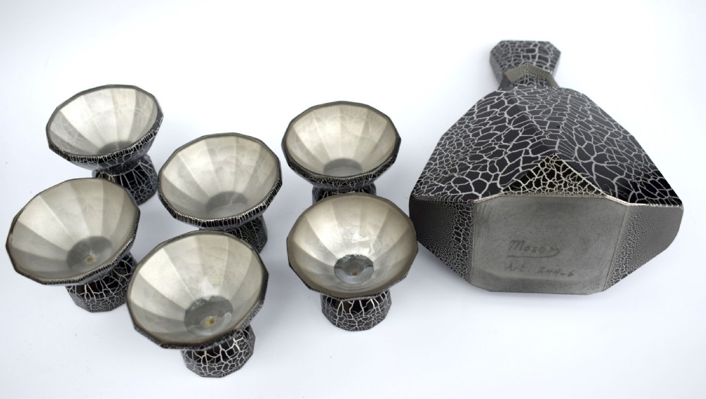An Art Deco black and silver crackle-patterned glass decanter with six matching small cups arranged on a circular mirrored tray with wood handles. View XI