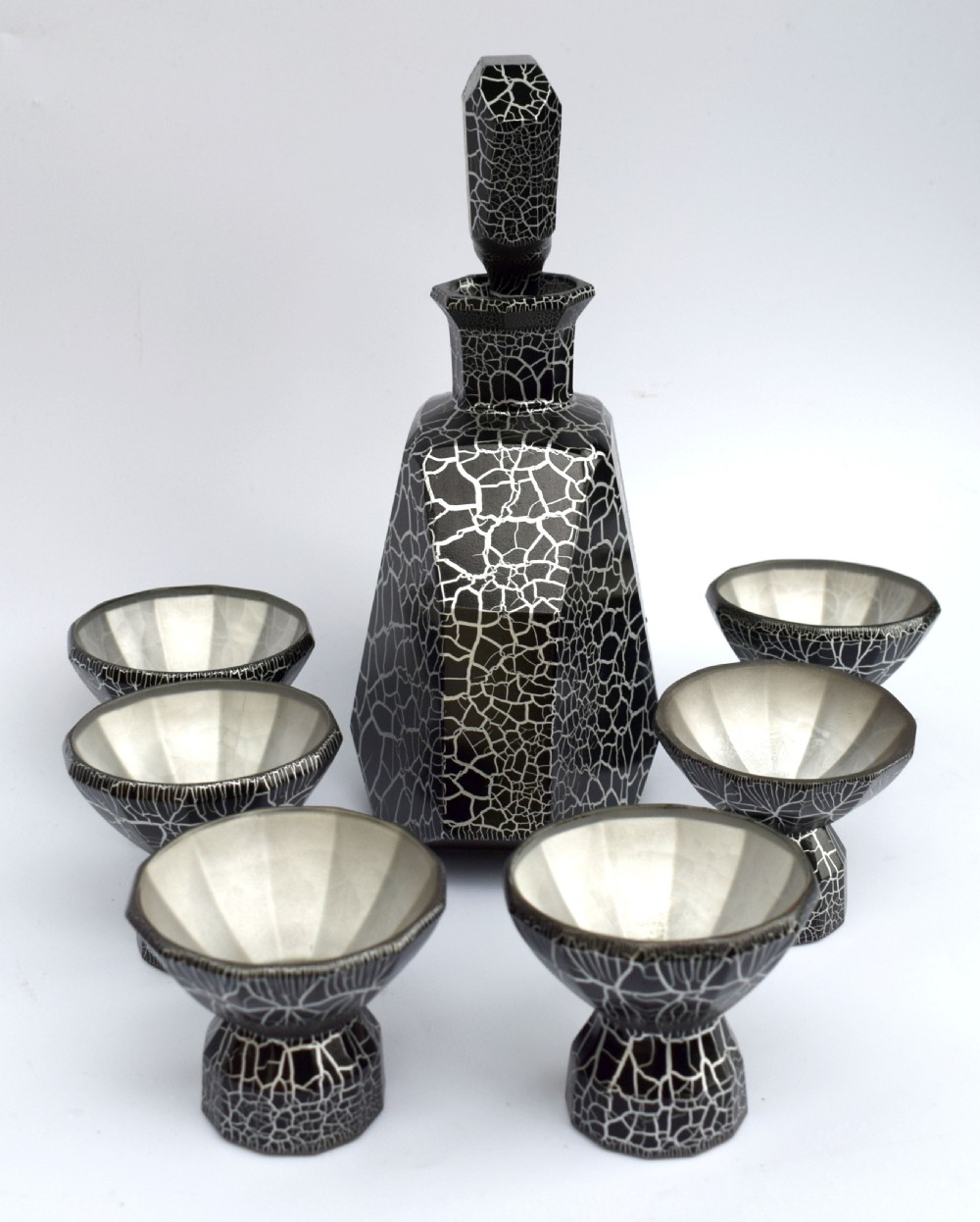 An Art Deco black and silver crackle-patterned glass decanter with six matching small cups arranged on a circular mirrored tray with wood handles. View XII