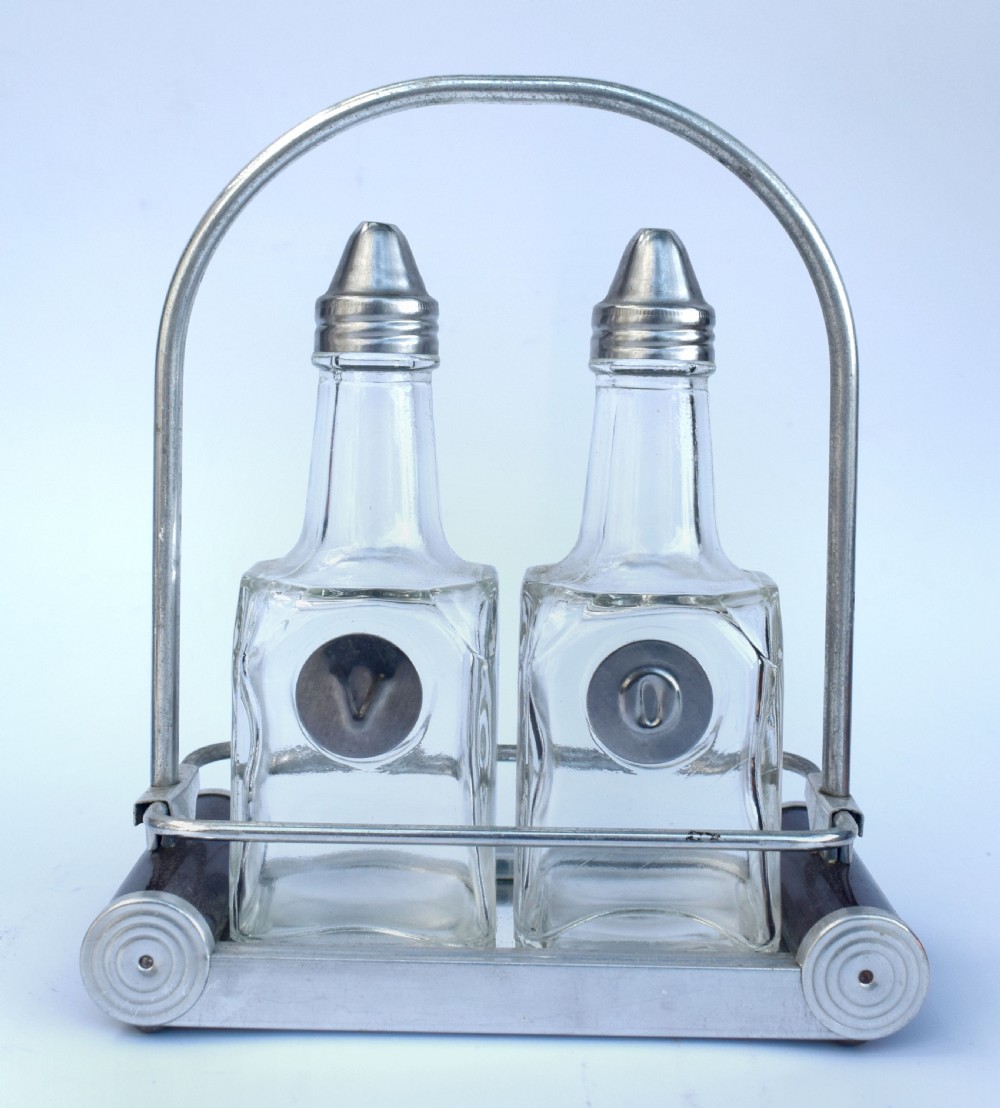 A pair of clear glass oil and vinegar bottles with silver metal tops marked V and O, housed in an Art Deco chrome carrying caddy. View VI