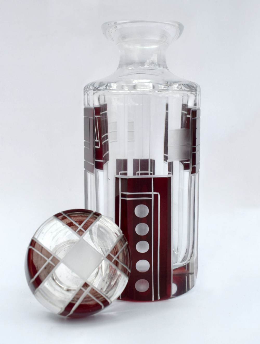 An Art Deco clear glass perfume bottle featuring geometric ruby red cut-to-clear overlay patterns and a matching round glass stopper. View II
