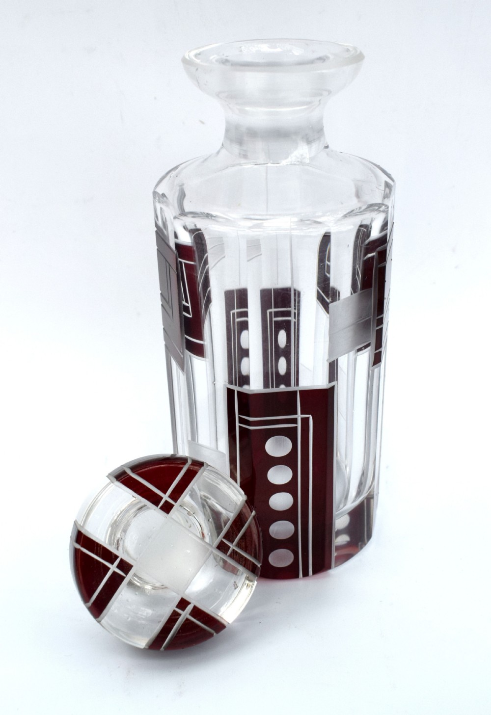 An Art Deco clear glass perfume bottle featuring geometric ruby red cut-to-clear overlay patterns and a matching round glass stopper. View V