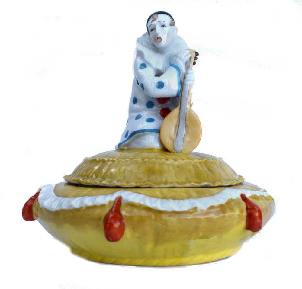 A yellow glazed porcelain powder bowl topped with a lid sculpted as a Pierrot character kneeling and playing a lute.
