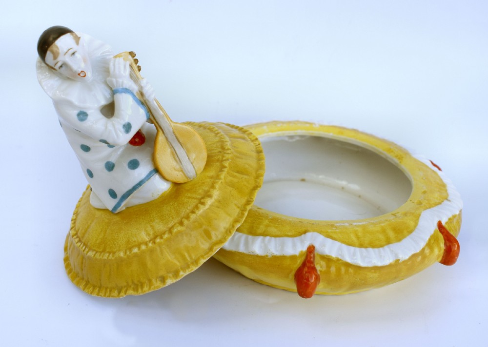 A yellow glazed porcelain powder bowl topped with a lid sculpted as a Pierrot character kneeling and playing a lute. View II