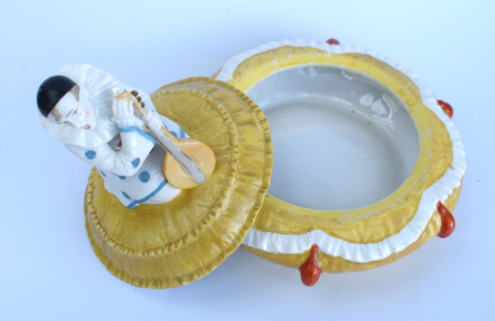 A yellow glazed porcelain powder bowl topped with a lid sculpted as a Pierrot character kneeling and playing a lute. View III