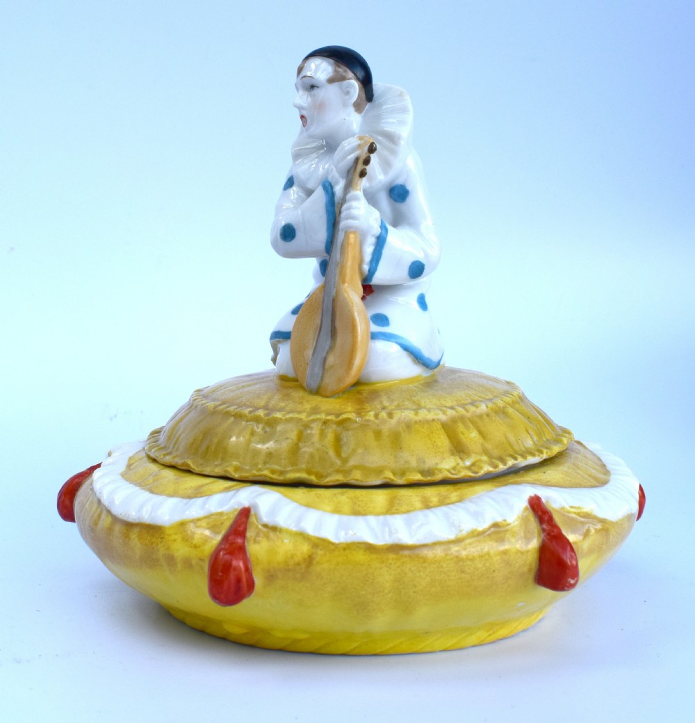 A yellow glazed porcelain powder bowl topped with a lid sculpted as a Pierrot character kneeling and playing a lute. View V