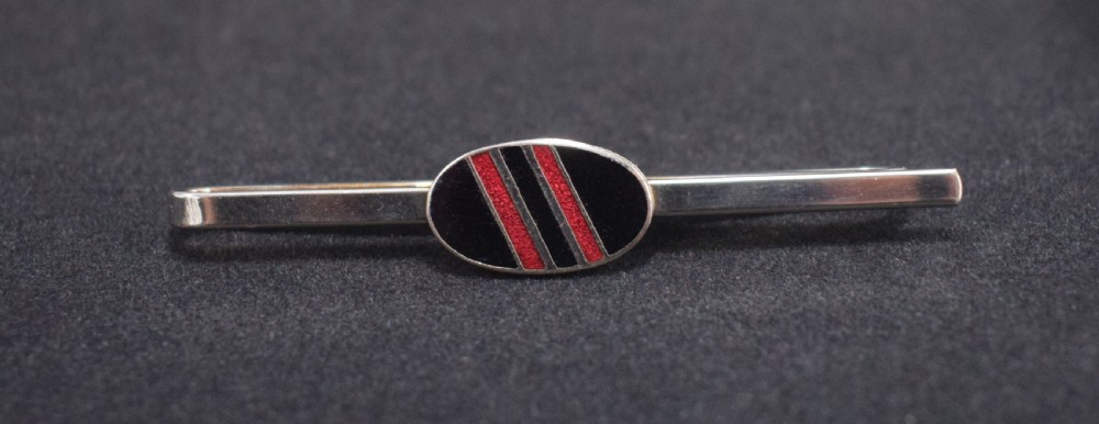 An Art Deco chrome tie slide featuring a central oval black and red enamelled plaque with diagonal stripes. View II