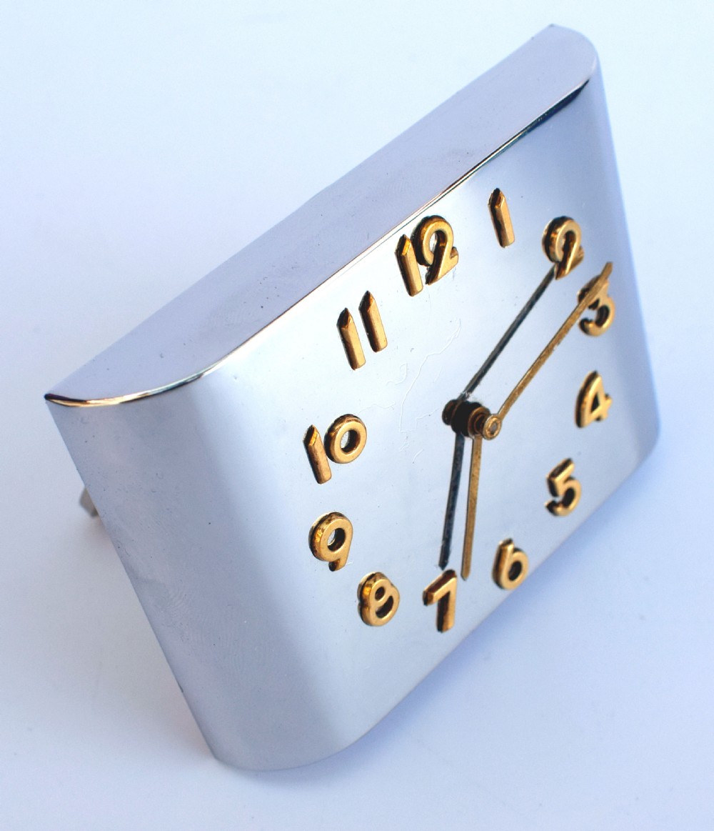 A curved rectangular chrome Art Deco travel clock featuring raised gold-coloured Arabic numerals and matching gold hands. View III