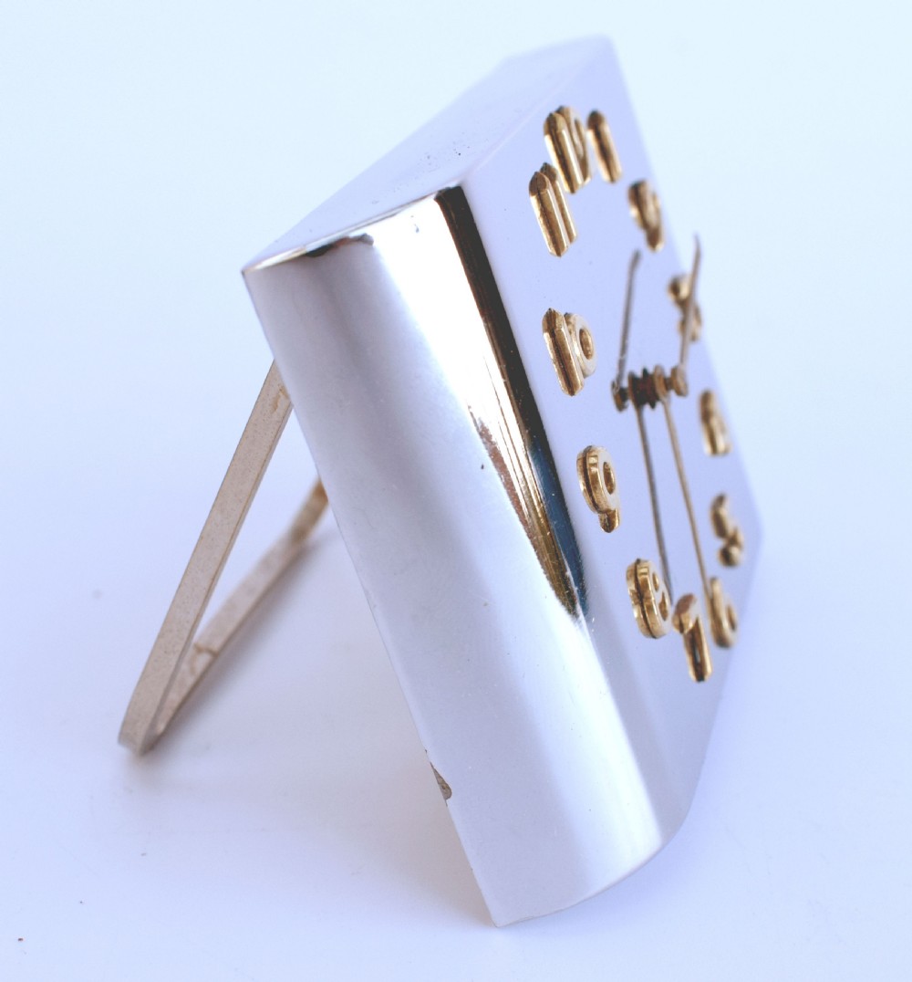 A curved rectangular chrome Art Deco travel clock featuring raised gold-coloured Arabic numerals and matching gold hands. View IV