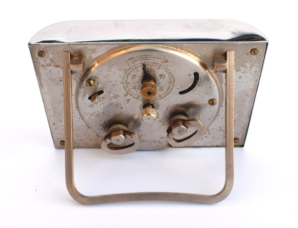 A curved rectangular chrome Art Deco travel clock featuring raised gold-coloured Arabic numerals and matching gold hands. View VI
