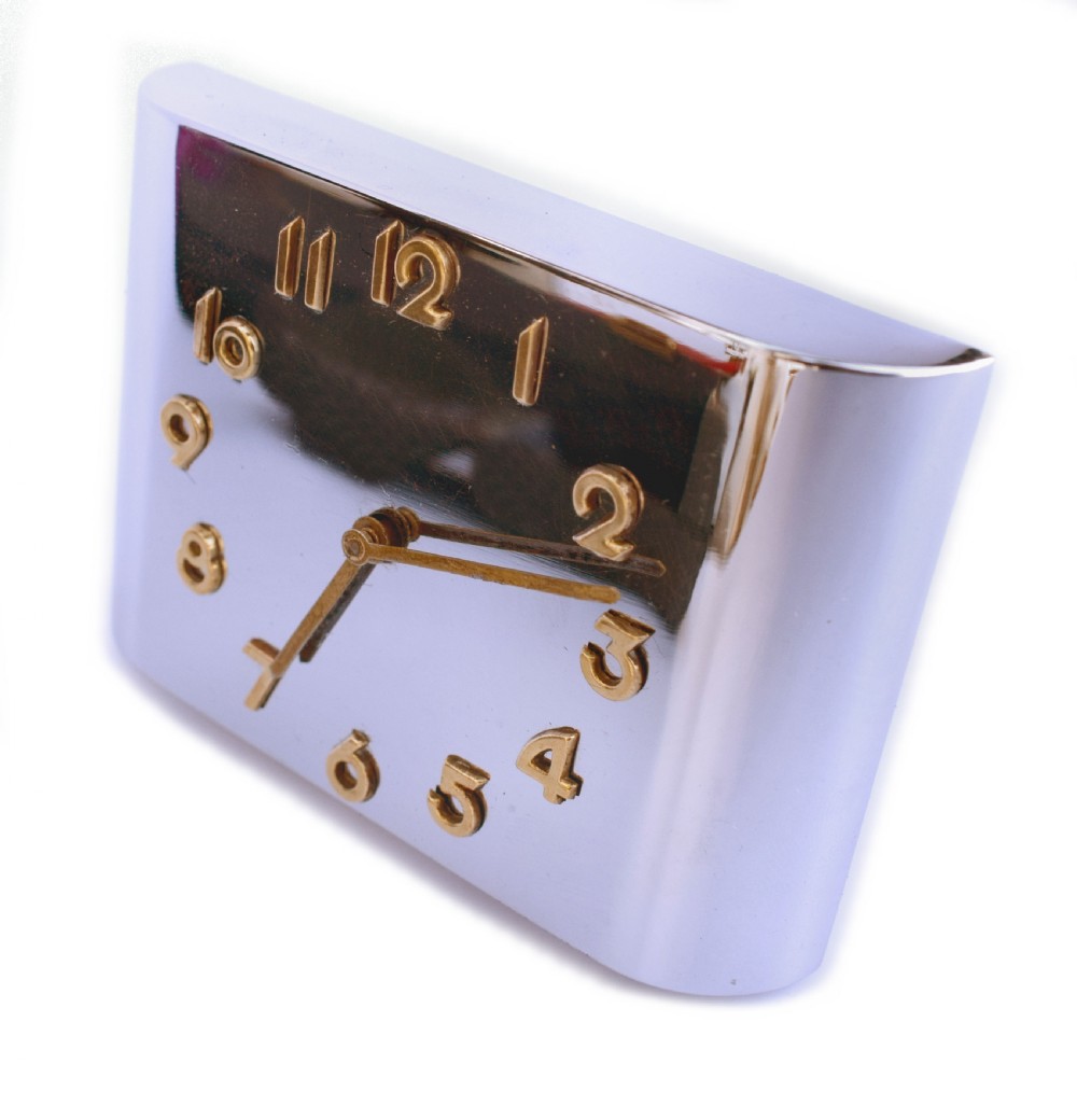 A curved rectangular chrome Art Deco travel clock featuring raised gold-coloured Arabic numerals and matching gold hands. View VII