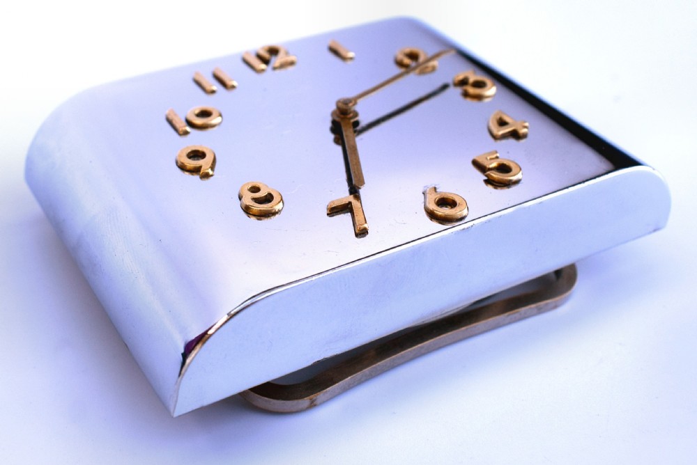A curved rectangular chrome Art Deco travel clock featuring raised gold-coloured Arabic numerals and matching gold hands. View VIII