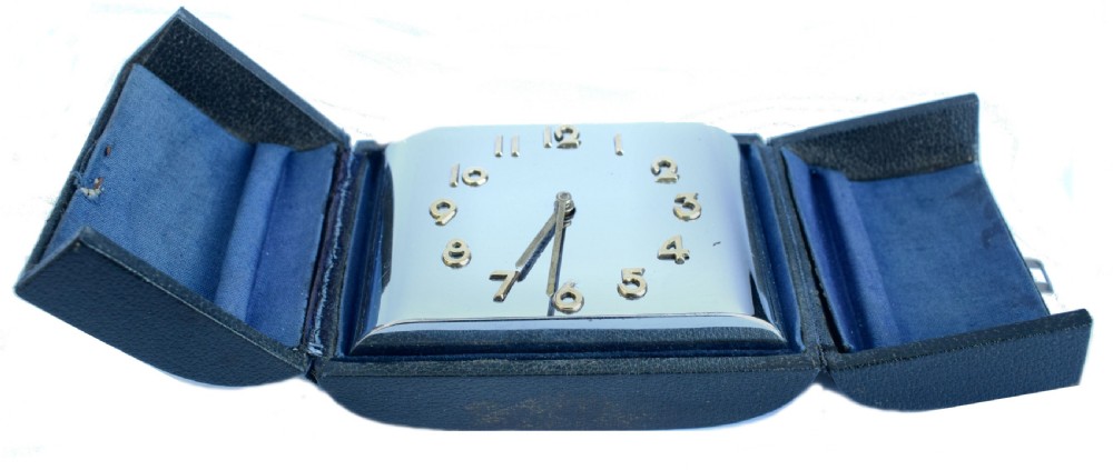 A curved rectangular chrome Art Deco travel clock featuring raised gold-coloured Arabic numerals and matching gold hands. View IX
