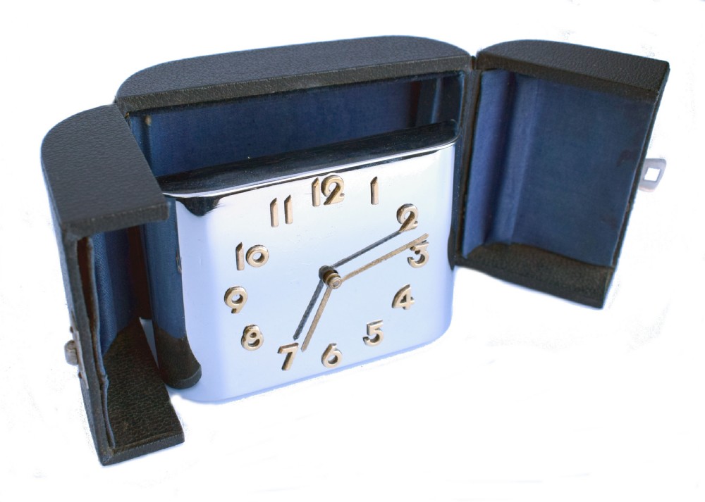 A curved rectangular chrome Art Deco travel clock featuring raised gold-coloured Arabic numerals and matching gold hands. View X