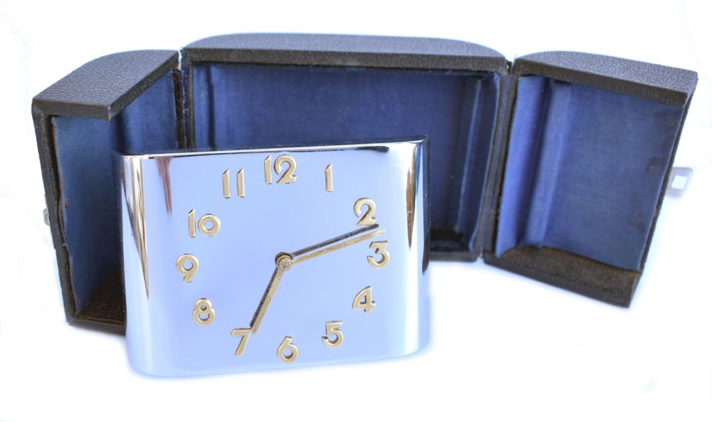 A curved rectangular chrome Art Deco travel clock featuring raised gold-coloured Arabic numerals and matching gold hands. View XI