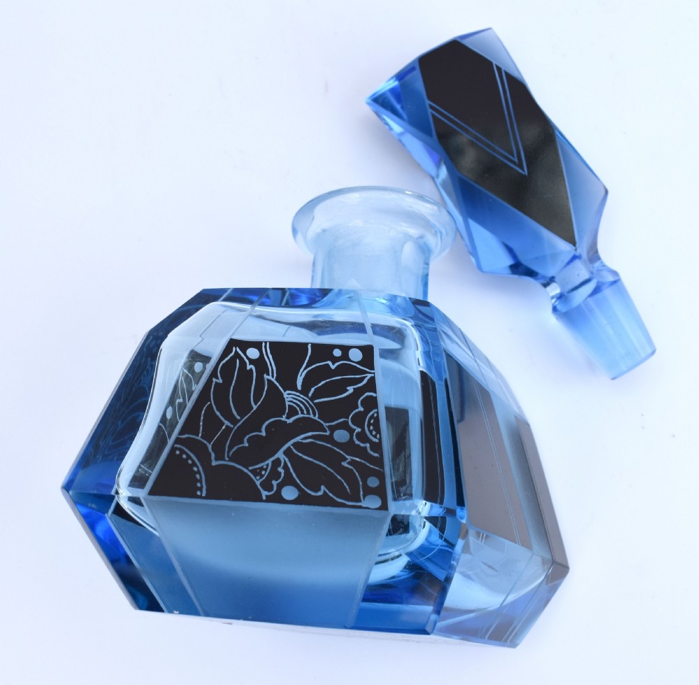 A blue Art Deco glass perfume bottle featuring geometric cut facets, black enamelled panels with etched floral designs, and a tall angular stopper. View V