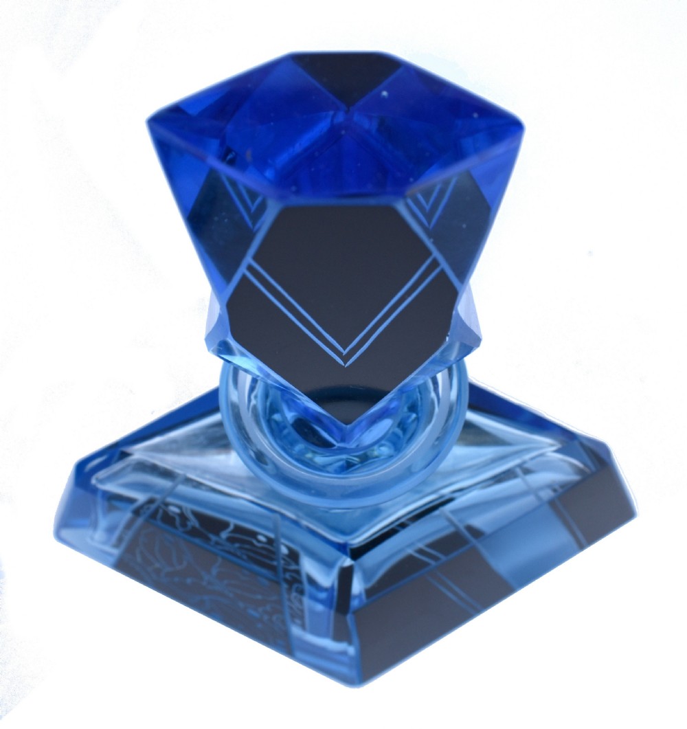 A blue Art Deco glass perfume bottle featuring geometric cut facets, black enamelled panels with etched floral designs, and a tall angular stopper. View VI