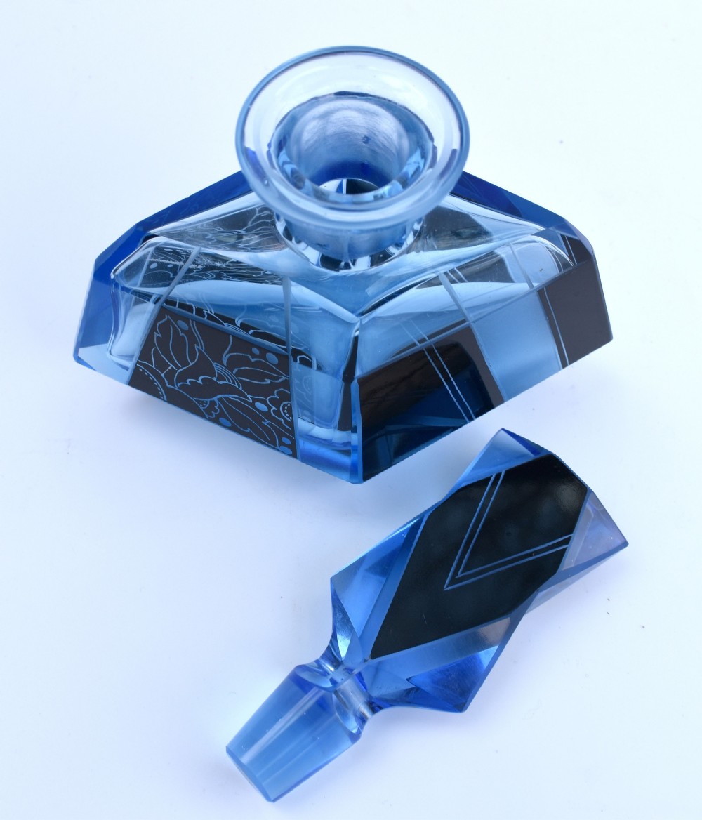 A blue Art Deco glass perfume bottle featuring geometric cut facets, black enamelled panels with etched floral designs, and a tall angular stopper. View VII