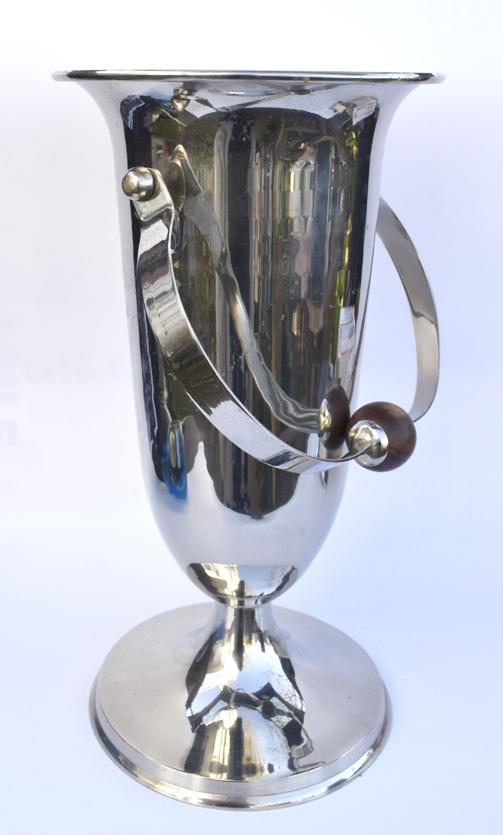 A tall polished chrome ice bucket featuring a pedestal base, flared top rim, and a curved swing handle with a turned wooden centre knob. View VII