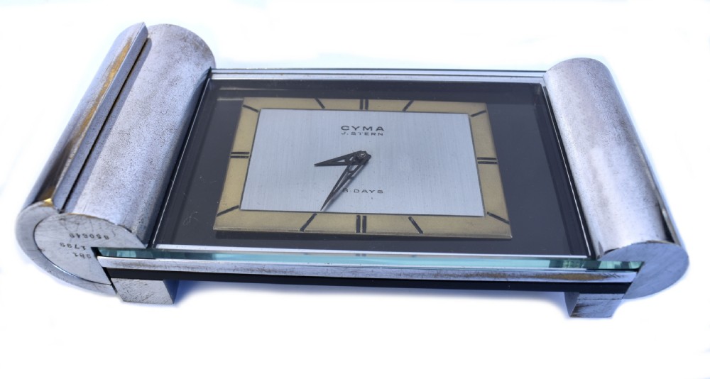 An Art Deco chrome desk clock featuring a rectangular face with geometric hour markers flanked by cylindrical chrome side pillars. View IV