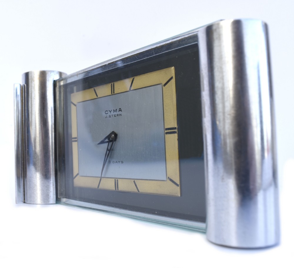 An Art Deco chrome desk clock featuring a rectangular face with geometric hour markers flanked by cylindrical chrome side pillars. View VI