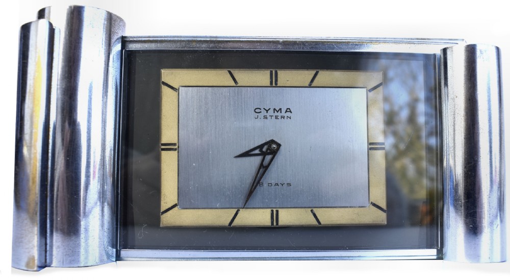 An Art Deco chrome desk clock featuring a rectangular face with geometric hour markers flanked by cylindrical chrome side pillars. View VII