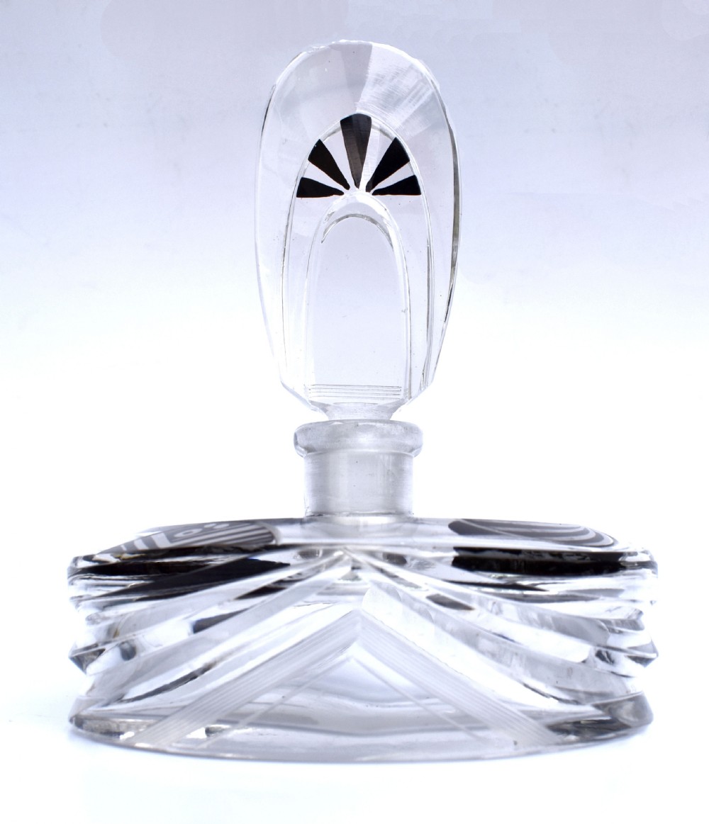 An Art Deco clear glass perfume bottle with angular cut facets, black enamelled fan details, and a matching tall stopper.