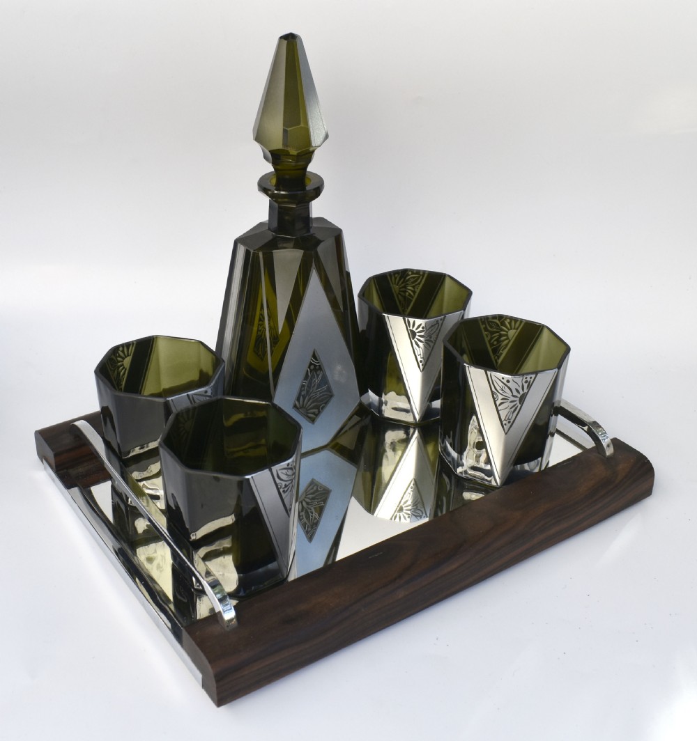 An Art Deco olive green glass decanter set featuring a faceted pyramidal bottle with a matching geometric stopper and six small angular tumblers etched with triangular patterns. View III
