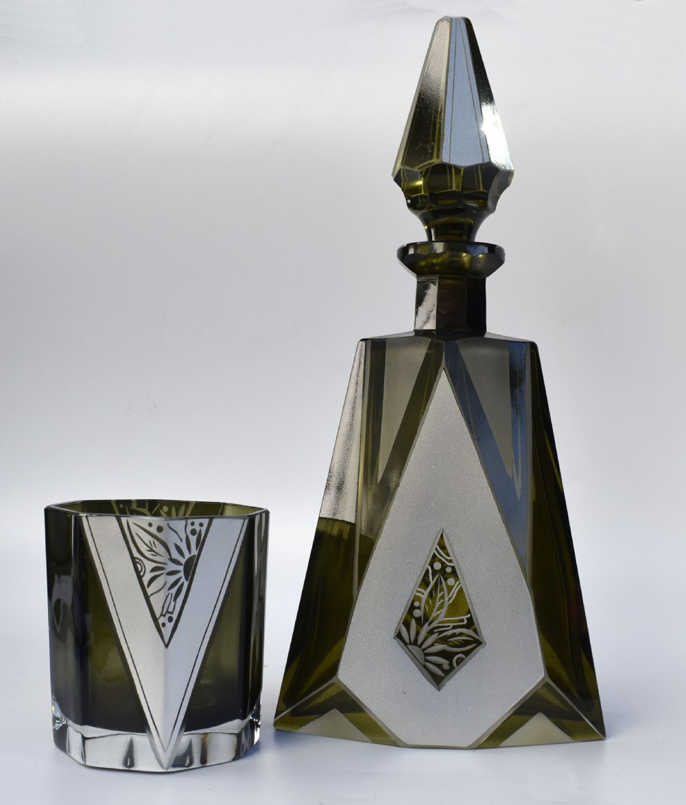 An Art Deco olive green glass decanter set featuring a faceted pyramidal bottle with a matching geometric stopper and six small angular tumblers etched with triangular patterns. View VI