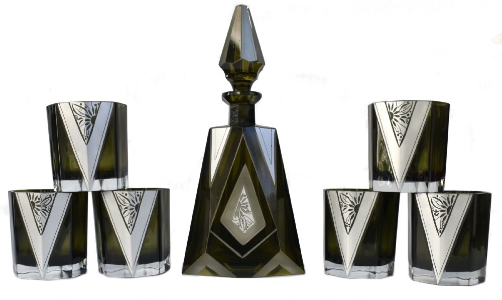 An Art Deco olive green glass decanter set featuring a faceted pyramidal bottle with a matching geometric stopper and six small angular tumblers etched with triangular patterns. View IX