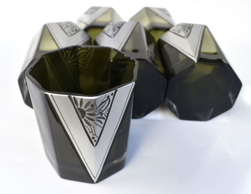 An Art Deco olive green glass decanter set featuring a faceted pyramidal bottle with a matching geometric stopper and six small angular tumblers etched with triangular patterns. View XI