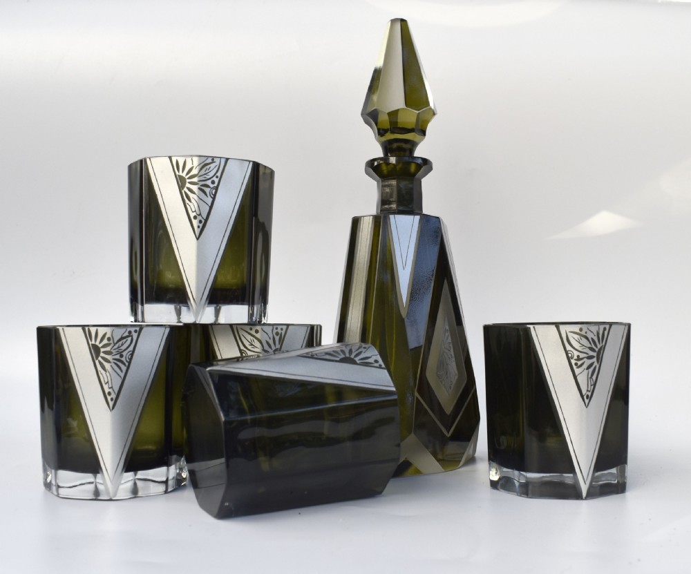An Art Deco olive green glass decanter set featuring a faceted pyramidal bottle with a matching geometric stopper and six small angular tumblers etched with triangular patterns. View XII