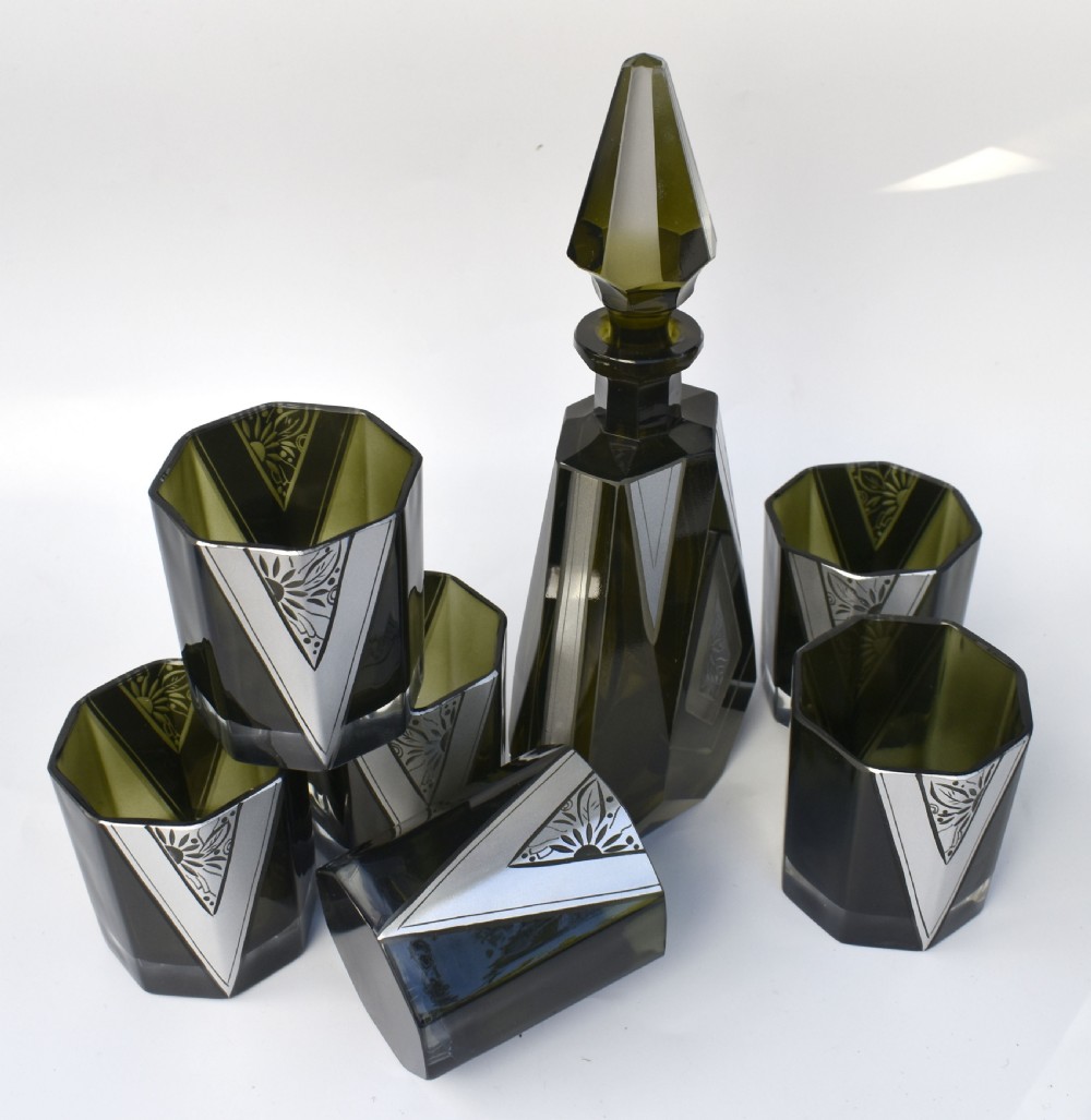 An Art Deco olive green glass decanter set featuring a faceted pyramidal bottle with a matching geometric stopper and six small angular tumblers etched with triangular patterns. View XIII