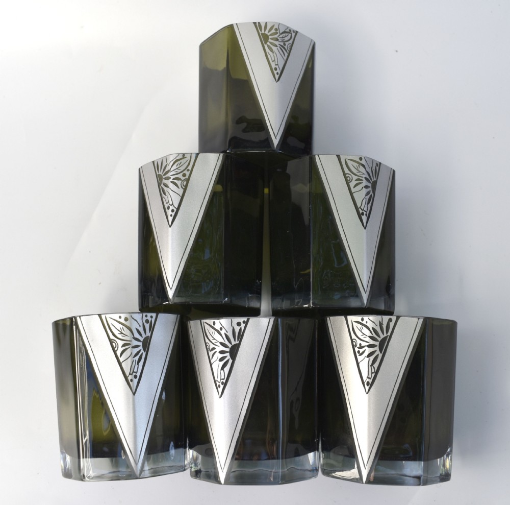An Art Deco olive green glass decanter set featuring a faceted pyramidal bottle with a matching geometric stopper and six small angular tumblers etched with triangular patterns. View XIV