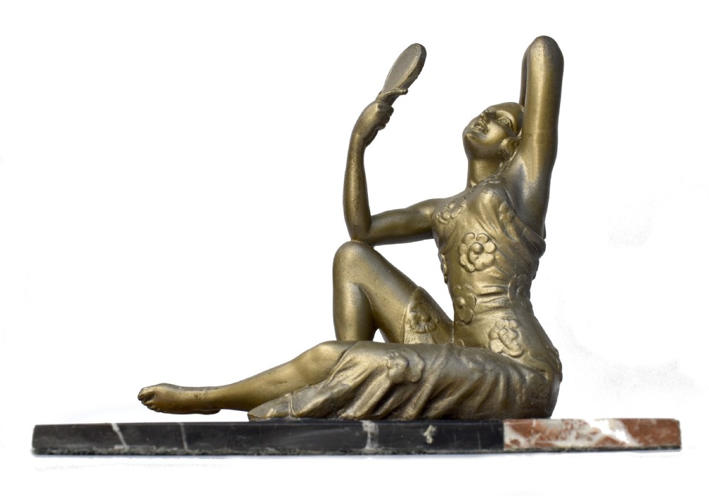 An Art Deco patinated metal figure of a seated woman holding a hand mirror, resting on a marble base.
