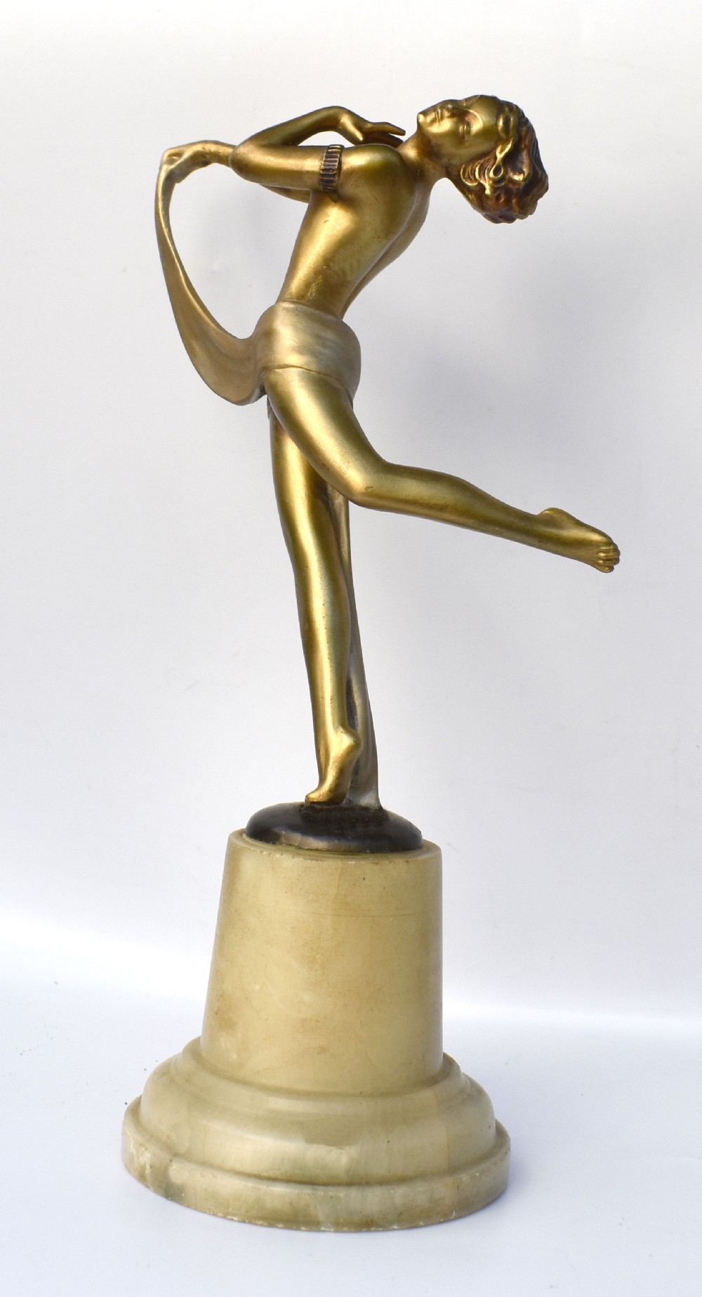 An Art Deco gold-tone spelter sculpture of a stylised female dancer set upon a turned cream alabaster base.