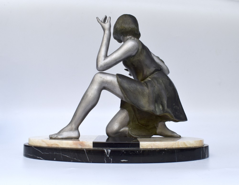 An Art Deco silver-toned spelter sculpture depicting a kneeling female figure holding a basket of coloured flowers, mounted on an oval cream onyx and black marble base. View V