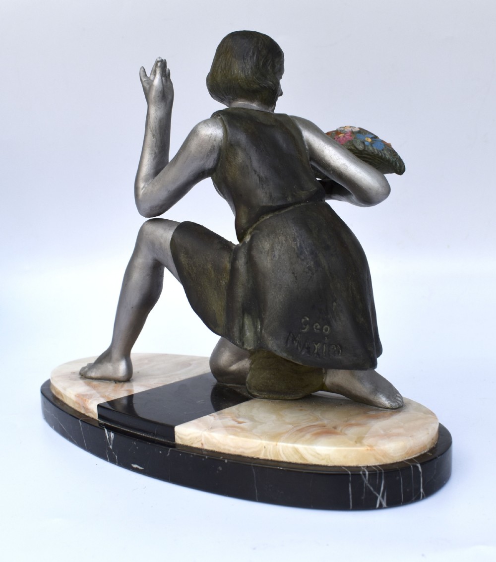An Art Deco silver-toned spelter sculpture depicting a kneeling female figure holding a basket of coloured flowers, mounted on an oval cream onyx and black marble base. View VI