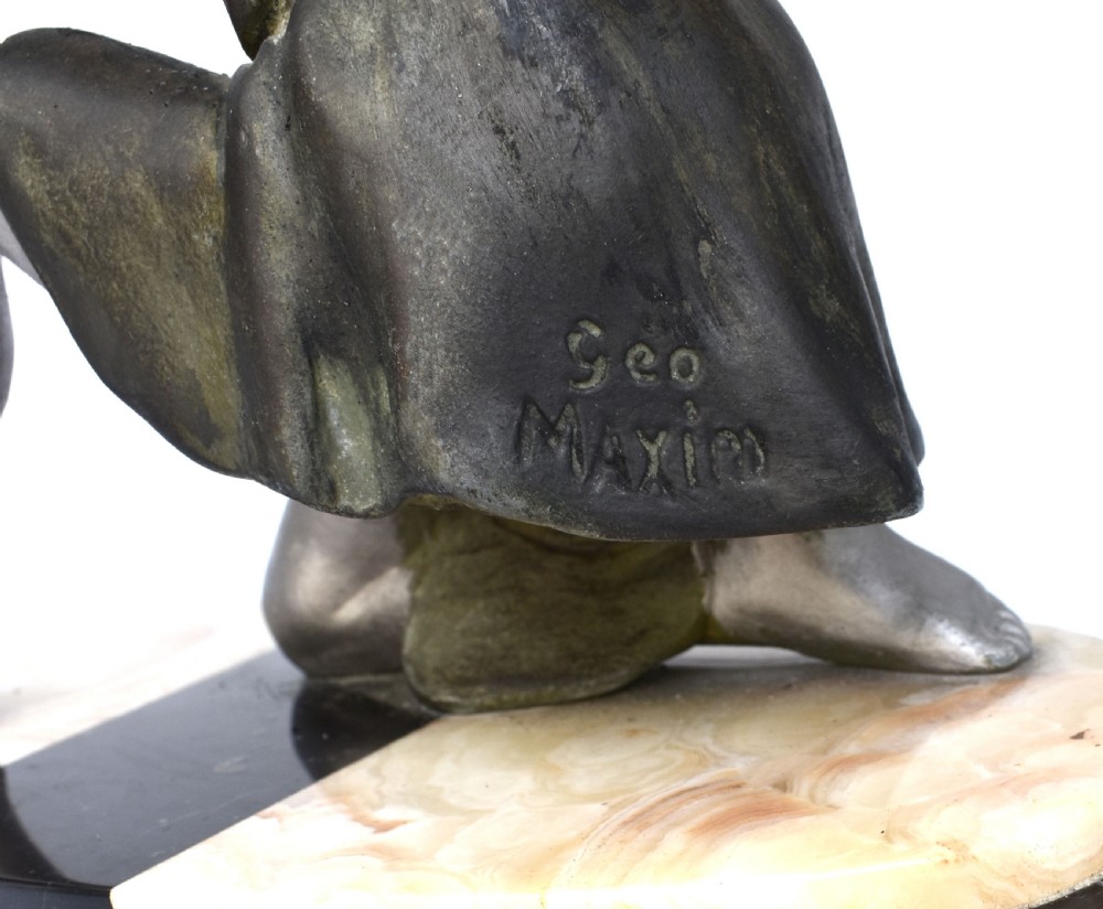 An Art Deco silver-toned spelter sculpture depicting a kneeling female figure holding a basket of coloured flowers, mounted on an oval cream onyx and black marble base. View VII