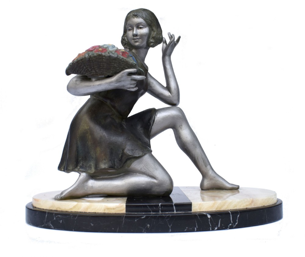 An Art Deco silver-toned spelter sculpture depicting a kneeling female figure holding a basket of coloured flowers, mounted on an oval cream onyx and black marble base. View IX
