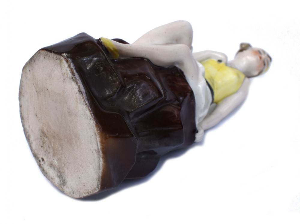 A hand-painted Art Deco ceramic hatpin holder depicting a bathing belle in a yellow top and yellow swim cap seated on a dark brown rock base. View VI