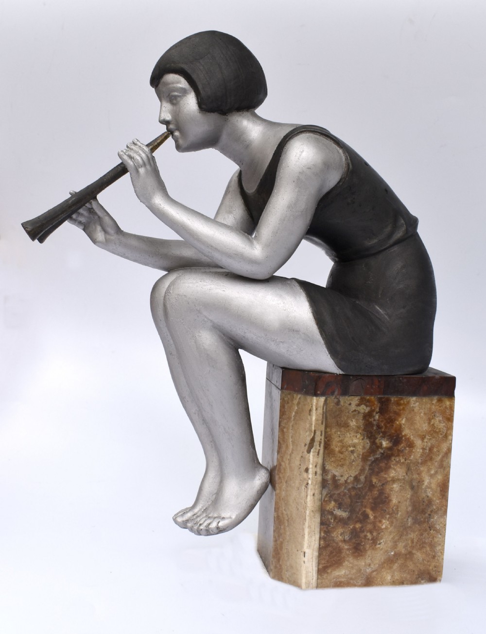 An Art Deco silver-painted spelter figure of a seated woman with short bobbed hair playing a pipe, positioned on a square brown onyx base. View IV