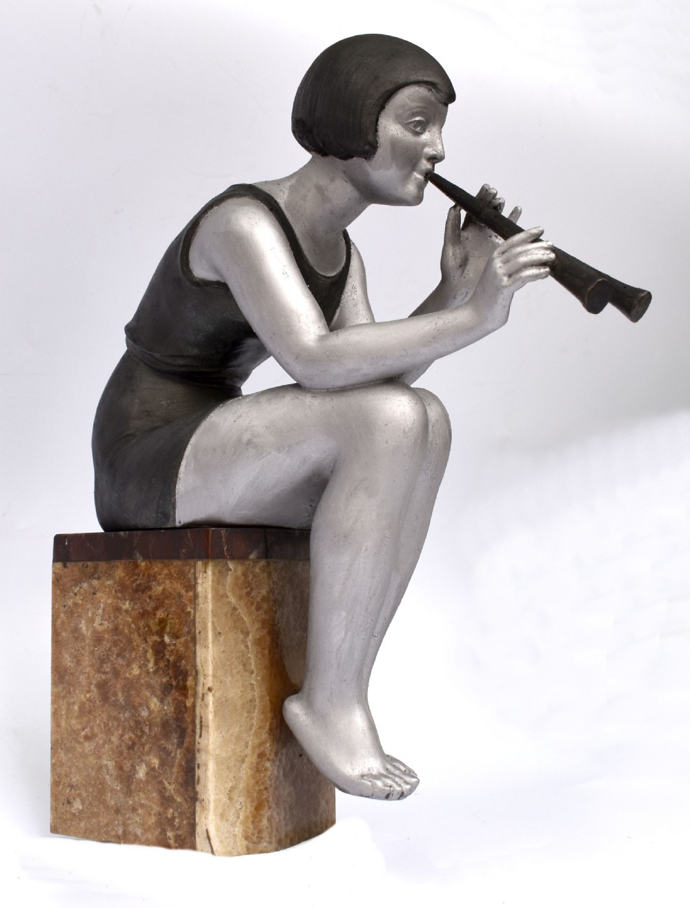An Art Deco silver-painted spelter figure of a seated woman with short bobbed hair playing a pipe, positioned on a square brown onyx base. View VI