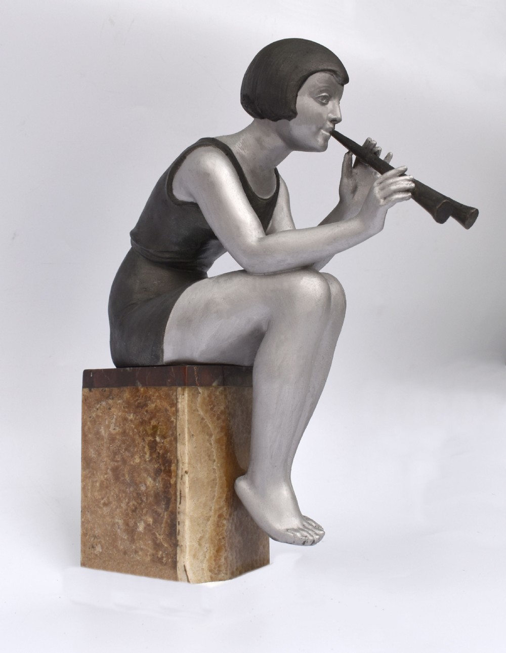 An Art Deco silver-painted spelter figure of a seated woman with short bobbed hair playing a pipe, positioned on a square brown onyx base. View VIII