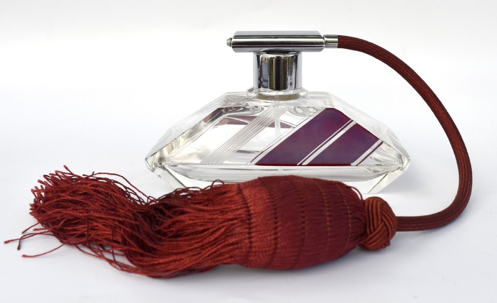 An Art Deco cut clear crystal glass perfume atomizer featuring a burgundy geometric inlay panel, chrome metal fitting, and a maroon fabric bulb with a fringe tassel.