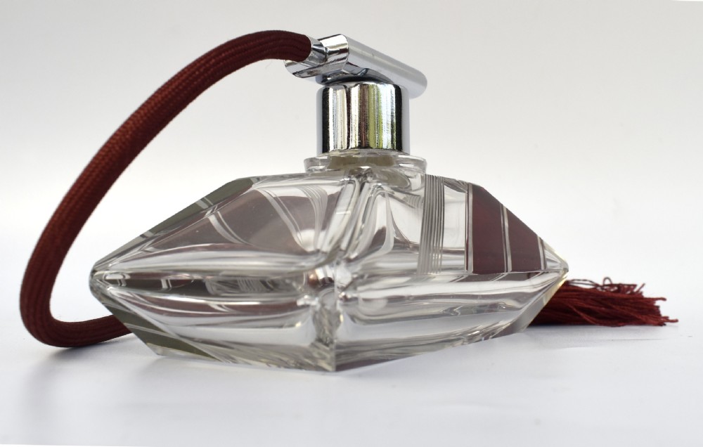 An Art Deco cut clear crystal glass perfume atomizer featuring a burgundy geometric inlay panel, chrome metal fitting, and a maroon fabric bulb with a fringe tassel. View IV