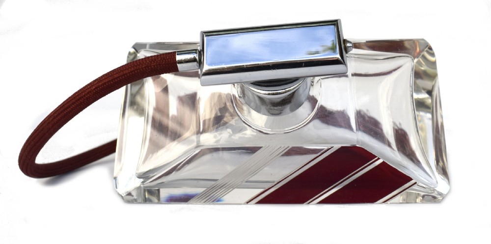 An Art Deco cut clear crystal glass perfume atomizer featuring a burgundy geometric inlay panel, chrome metal fitting, and a maroon fabric bulb with a fringe tassel. View VIII