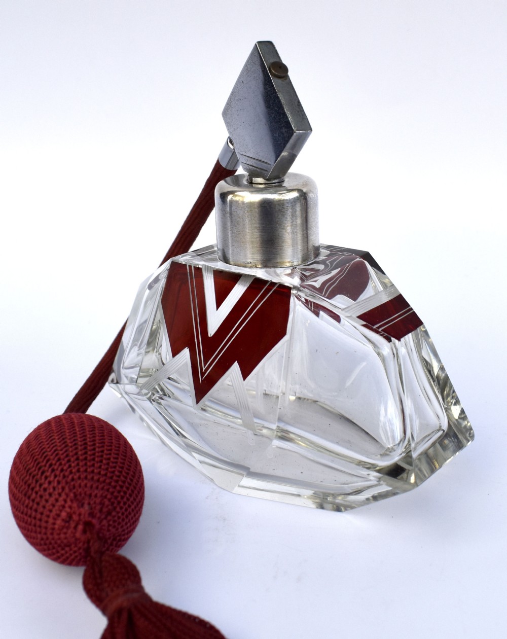 An Art Deco cut crystal perfume atomiser featuring burgundy geometric chevron detailing, chrome fittings, and a matching burgundy squeeze bulb with a long tassel. View III